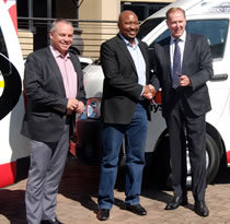 Three men shaking hands in front of a branded minibus at the vehicle handover.