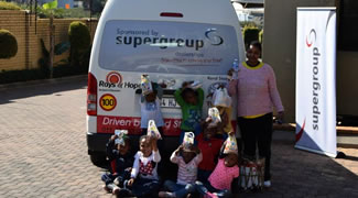 Children in costume seated in front of a Rays of Hope minibus sponsored by Super Group, with an adult standing beside them.