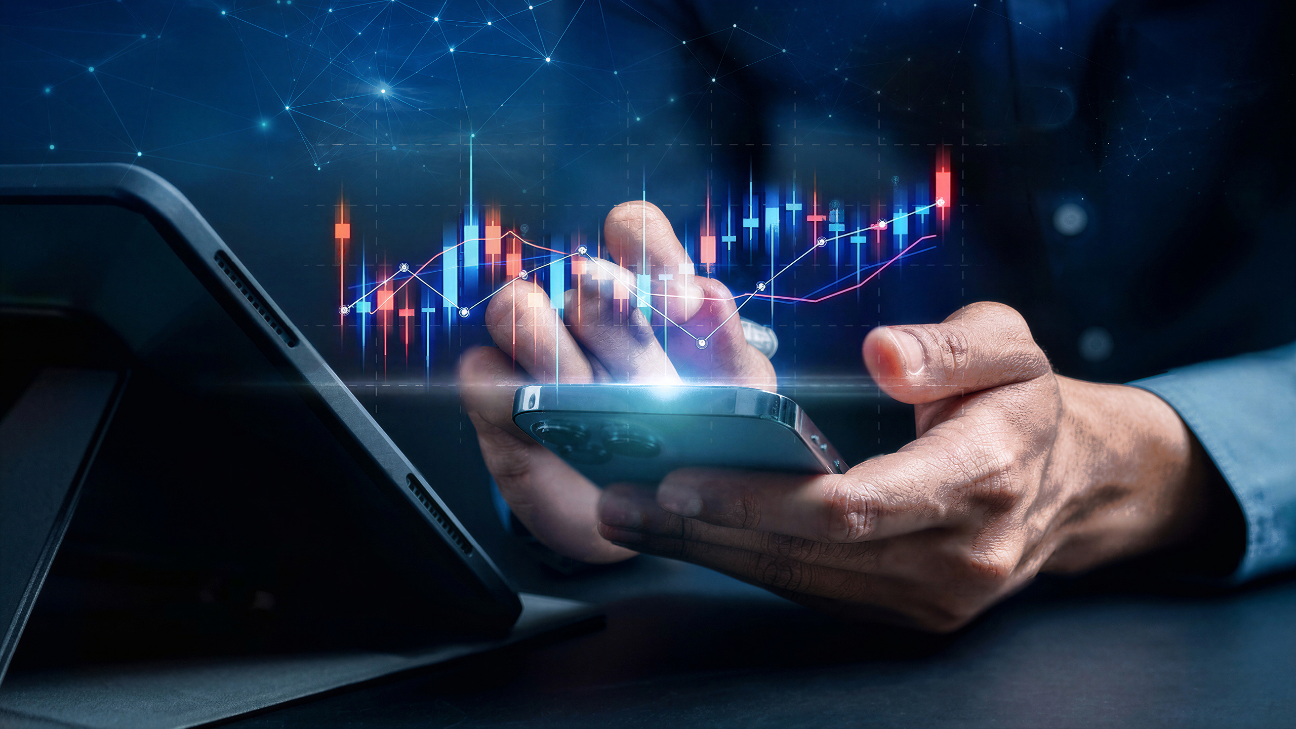 A hand holds a smartphone beside a tablet, with an unlabelled share price chart projected above the screen.