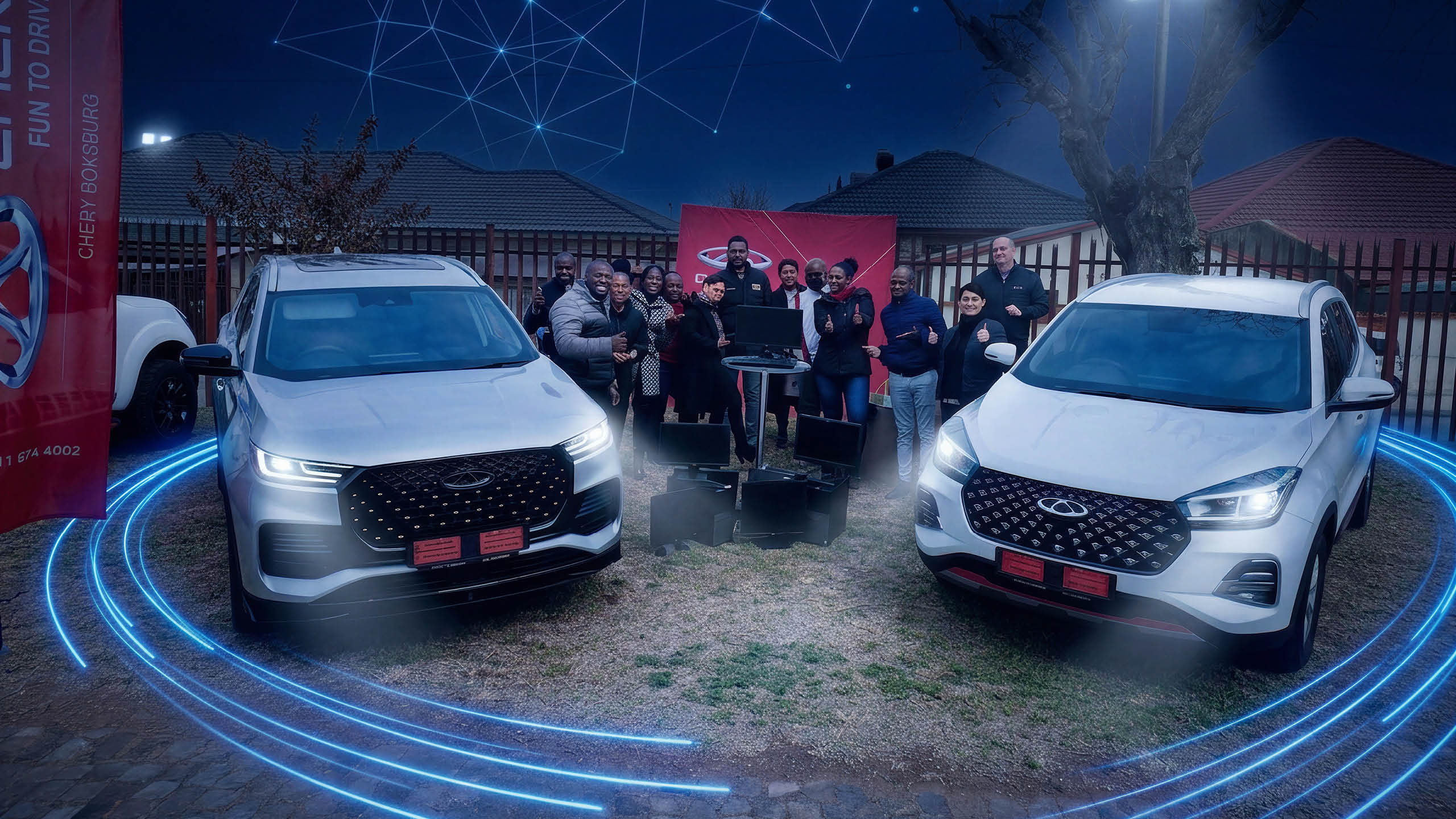 A group of people standing between two vehicles at a handover of donated computer equipment.